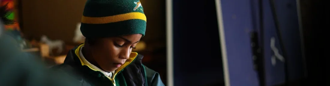 A child in a striped beanie and school jacket working quietly at a table