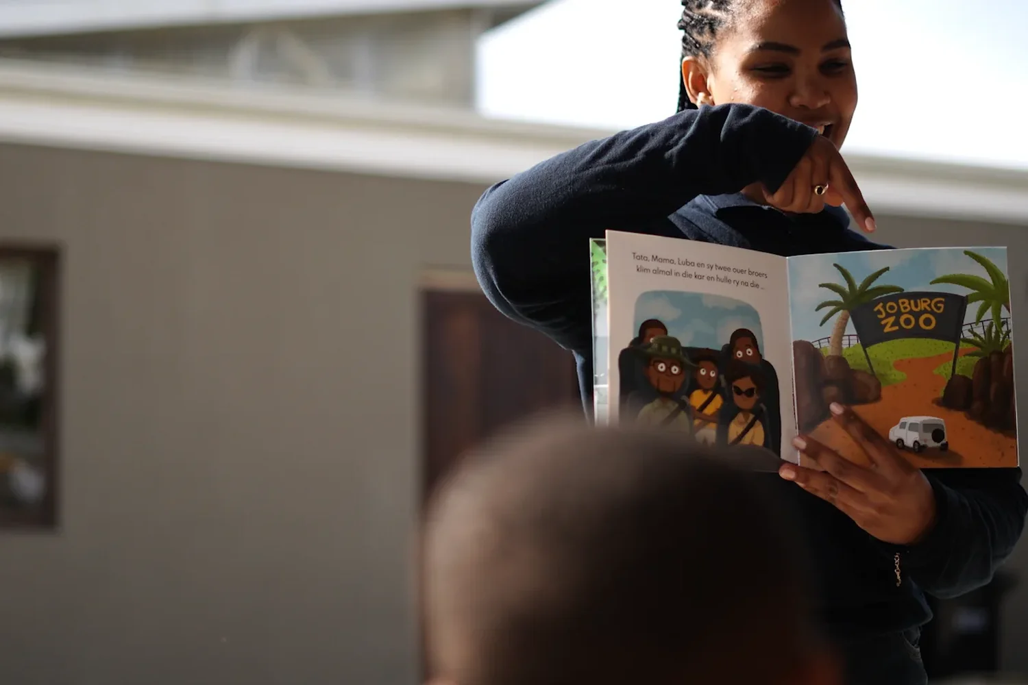 A volunteer holding an open picture book up so the children in front of her can see the page